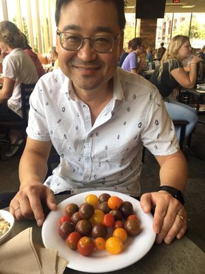 A man smiling over a plate of tomatoes.
