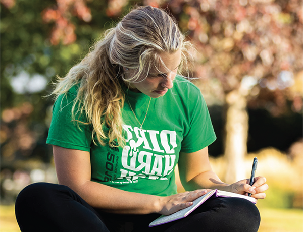 A student writing in a journal outdoors
