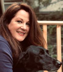 headshot of Beth Cash posing with large black dog