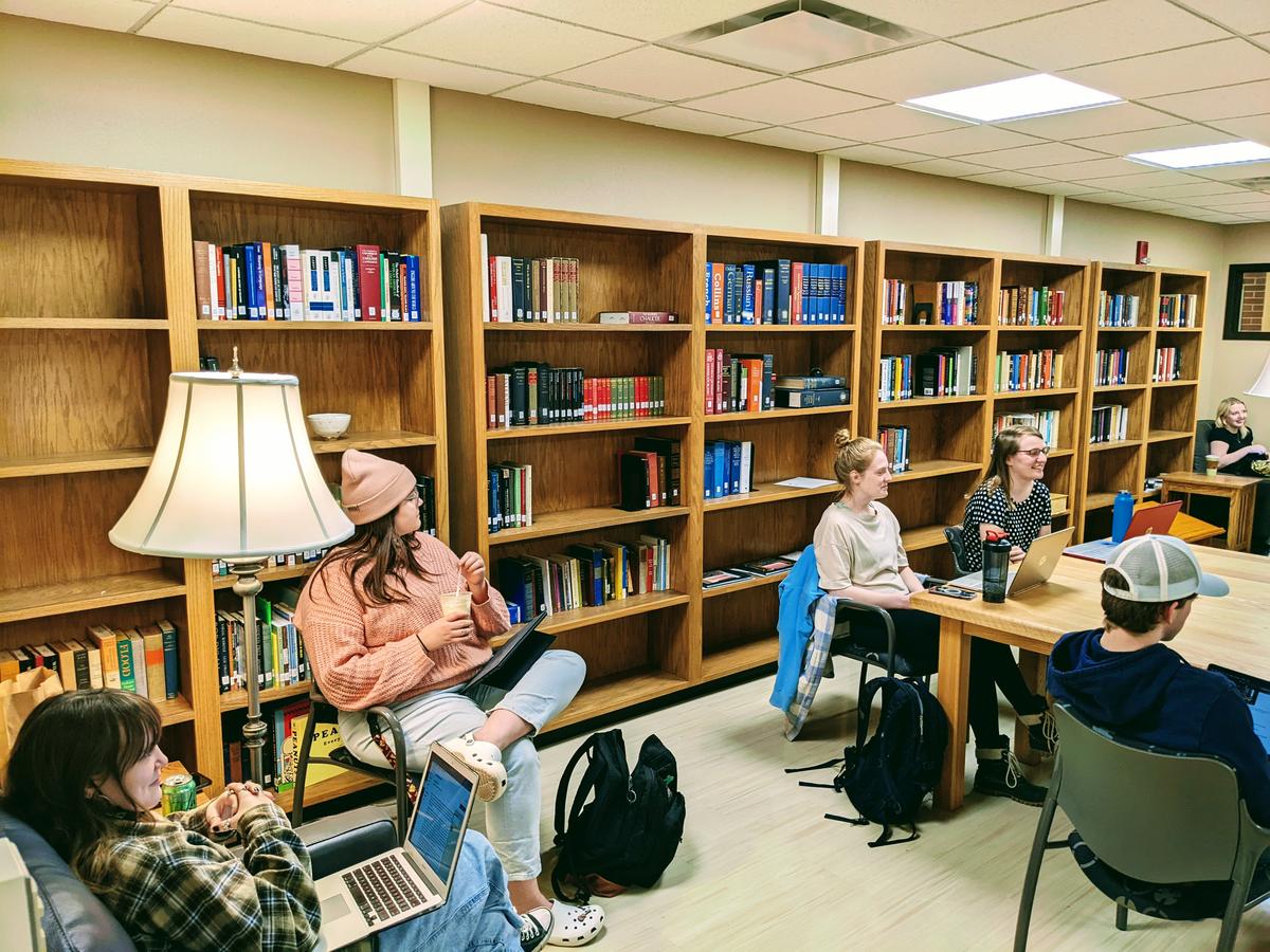 Students gathered seated in a small space with bookshelves lining walls