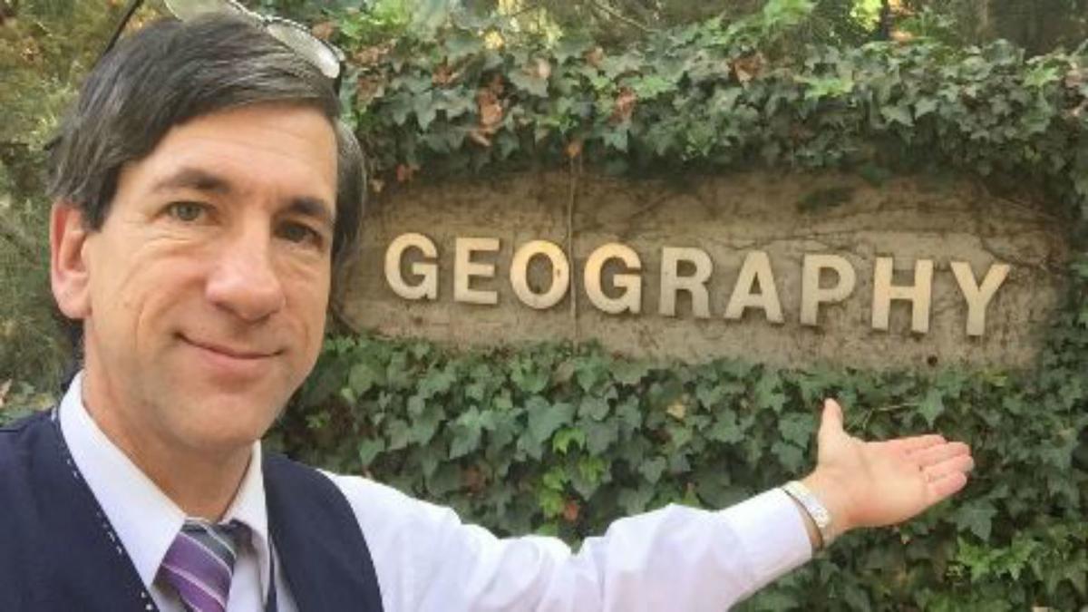 man pointing at an outdoor sign that reads "georgraphy"