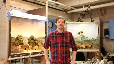 Photo of Aaron Delehanty with two landscape paintings